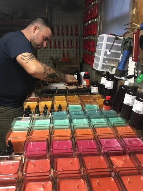 Ross Mingarelli hand-pouring soy candles in his original Concord NH workshop — rows of colorful hand-poured candles where CandleTree began